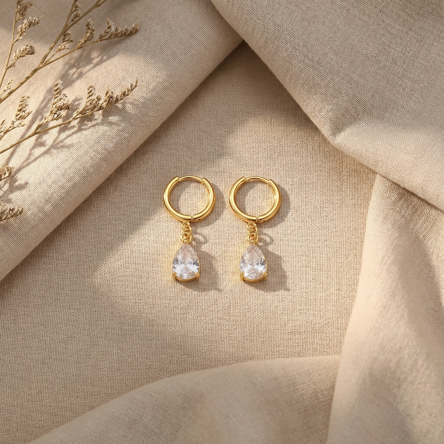 Gold earrings with teardrop-shaped crystals on a beige fabric background