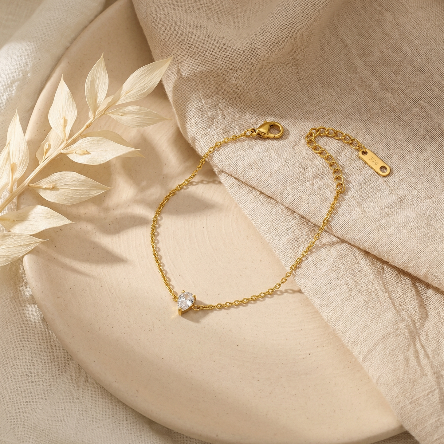 Gold teardrop-shaped bracelet with a small diamond on a beige fabric background