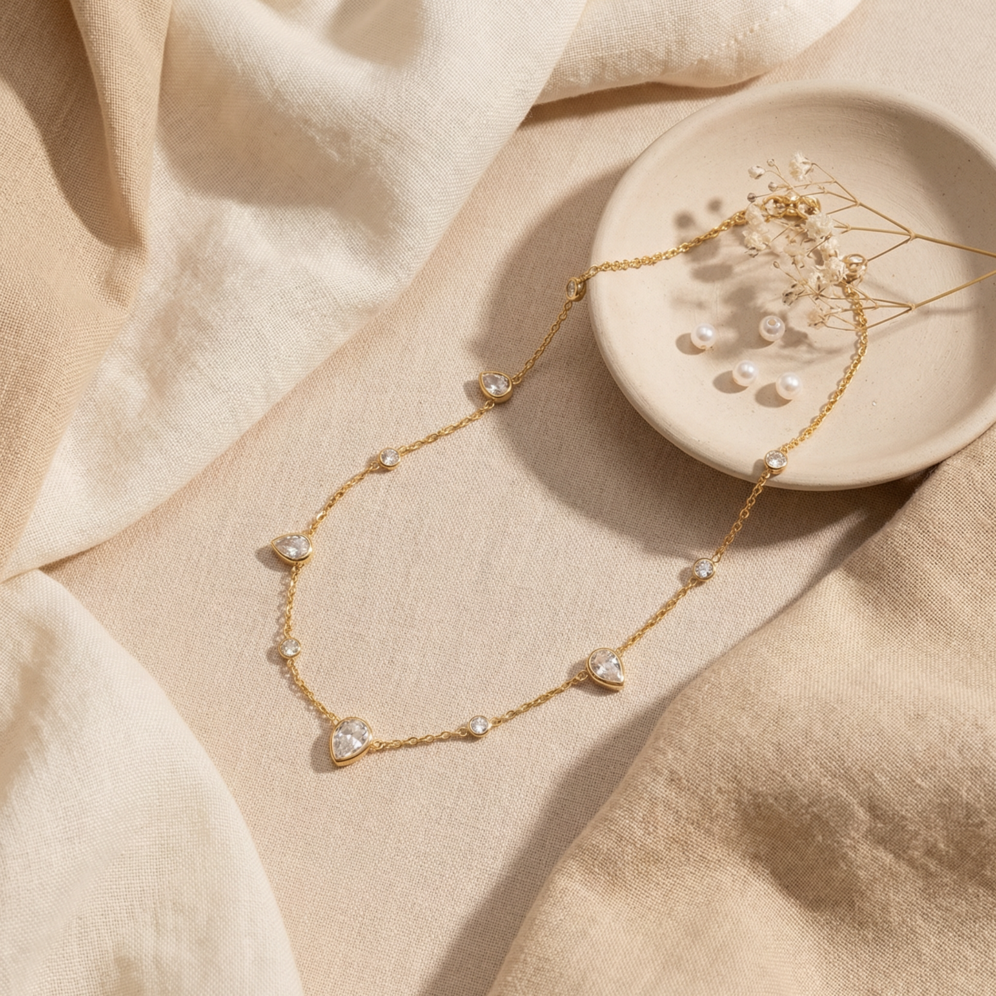Gold necklace with teardrop-shaped pendants on a beige fabric background