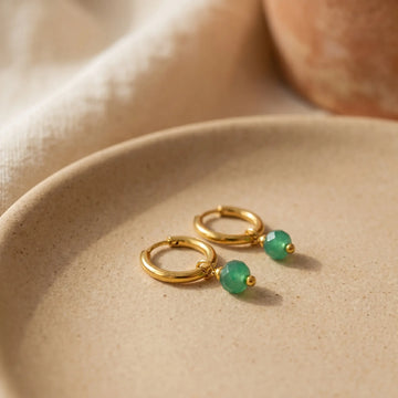 Earrings collection - gold huggie hoop earrings styled on a soft beige background