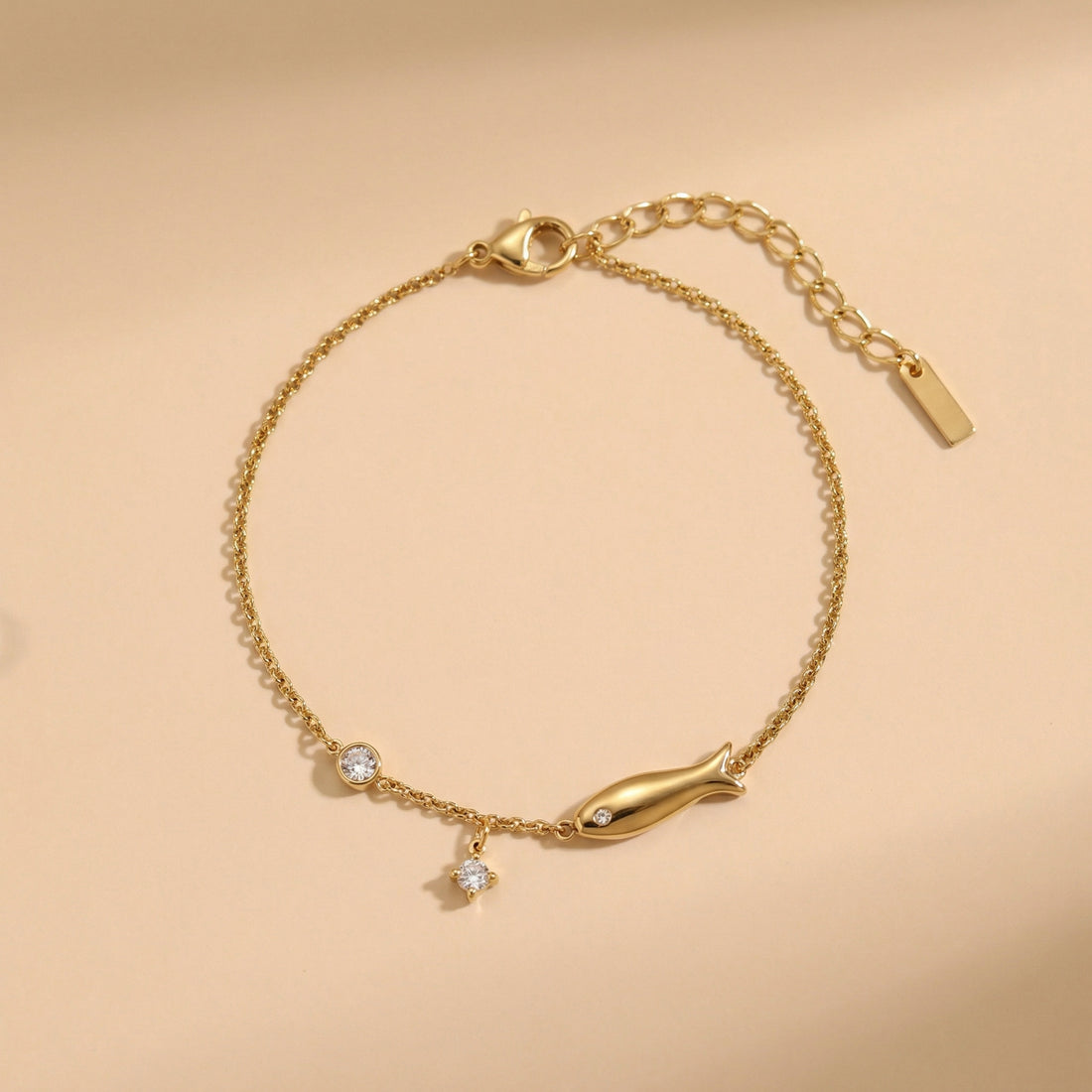 Gold bracelet with fish charm on a beige background