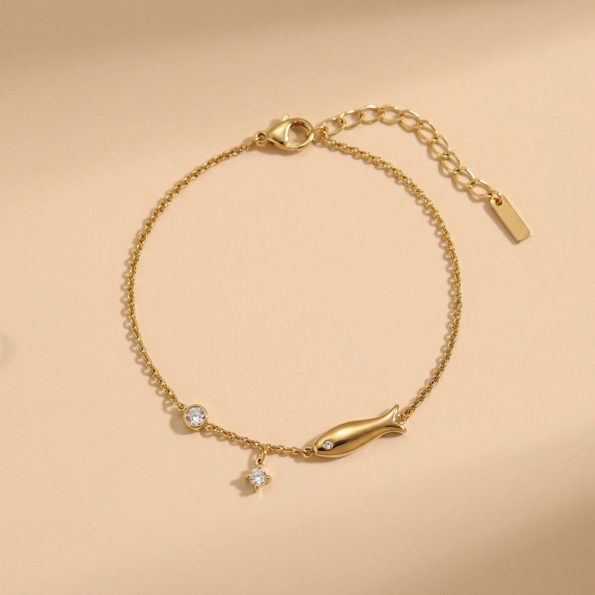 Gold bracelet with fish charm on a beige background