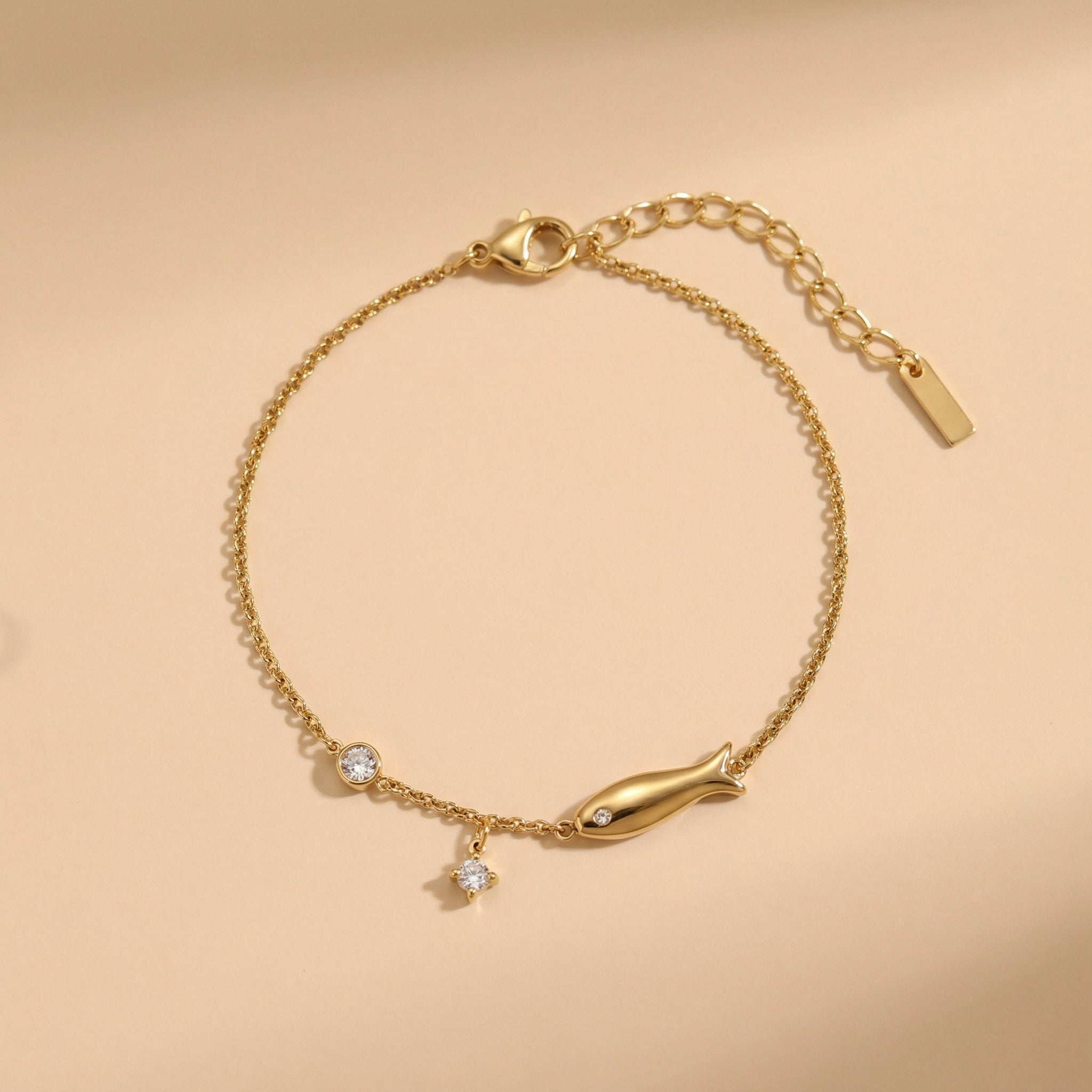Gold bracelet with fish charm on a beige background