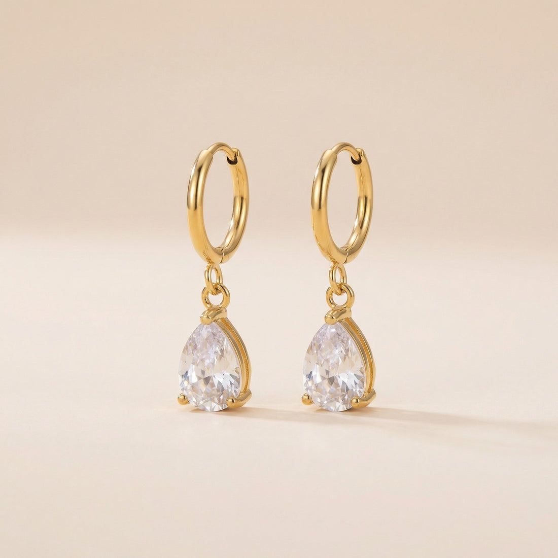Gold hoop earrings with teardrop-shaped gemstones on a beige background