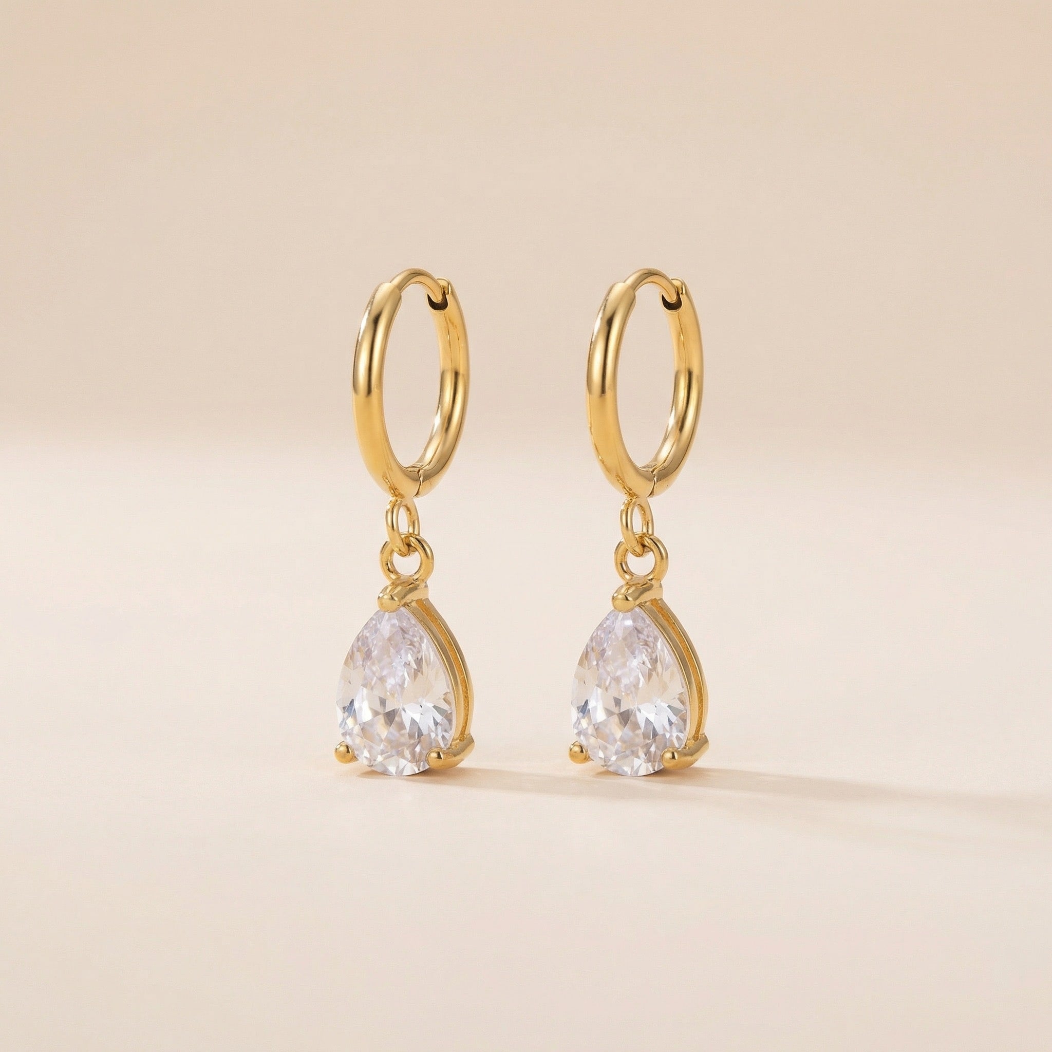 Gold hoop earrings with teardrop-shaped gemstones on a beige background