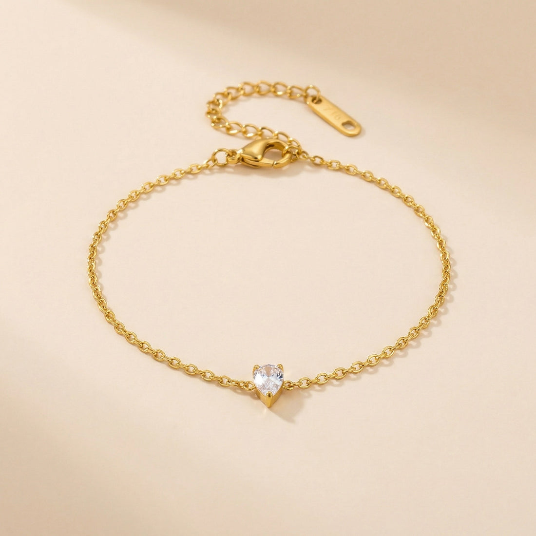 Gold bracelet with a teardrop-shaped crystal on a beige background