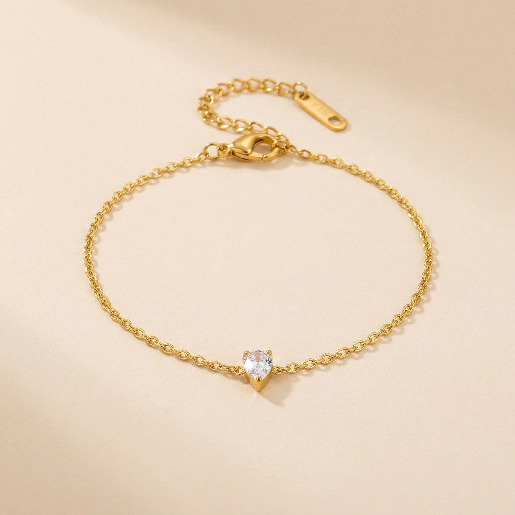 Gold bracelet with a teardrop-shaped crystal on a beige background