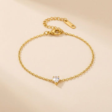 Gold bracelet with a teardrop-shaped crystal on a beige background