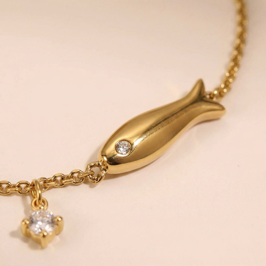 Gold bracelet with fish charm on a beige background