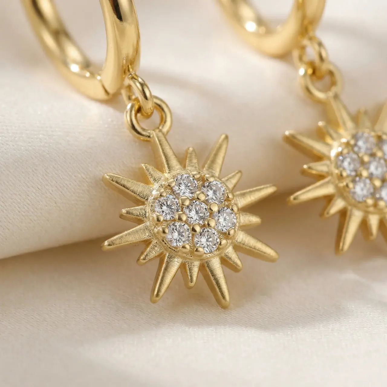 Gold hoop earrings with star-shaped diamond pendants on a beige background