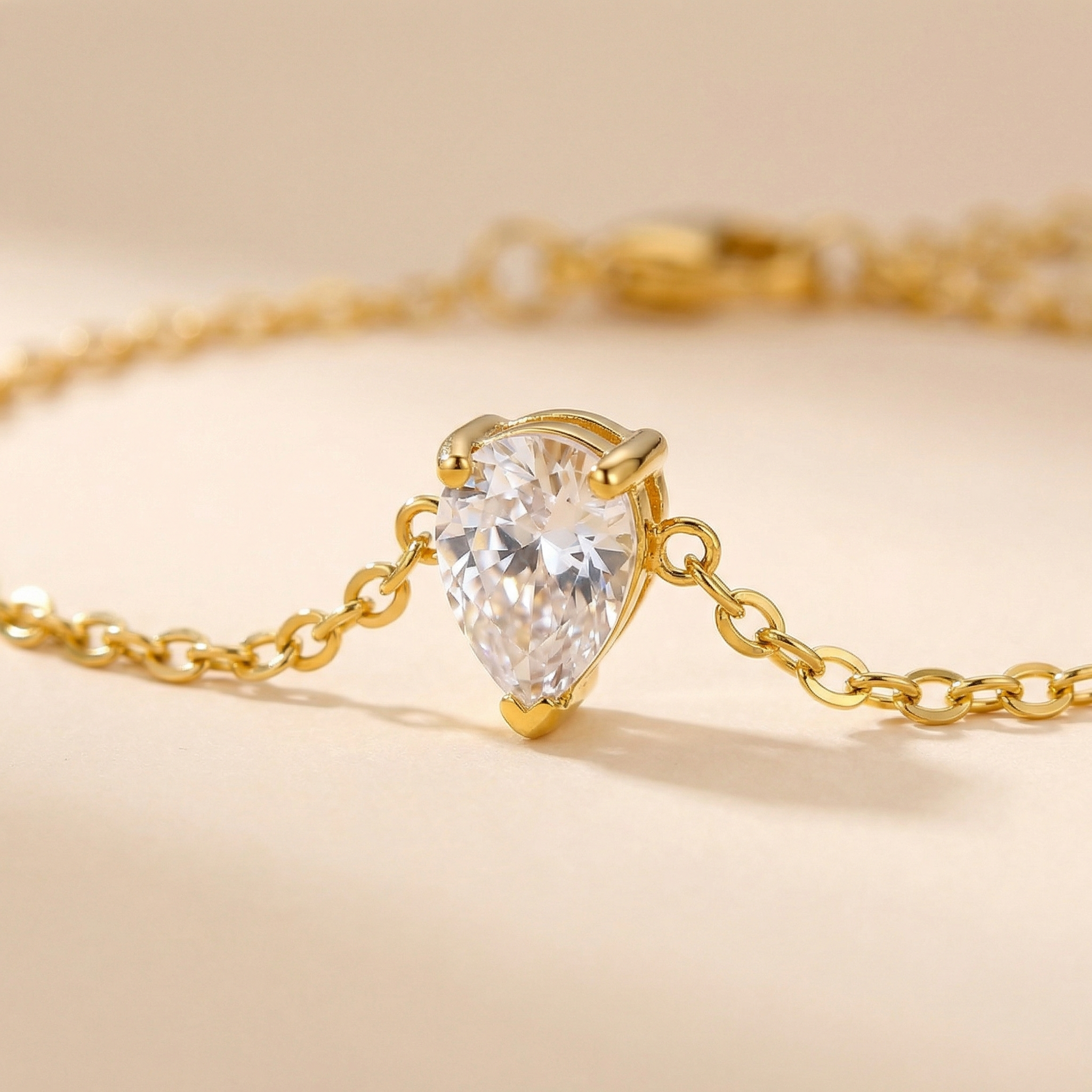 Gold necklace with a teardrop-shaped diamond pendant on a beige background