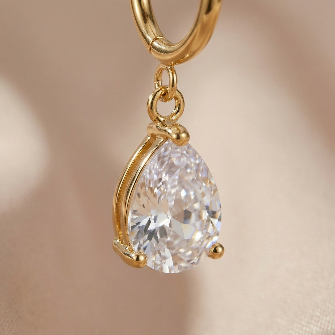 Gold hoop earrings with teardrop-shaped gemstones on a beige background