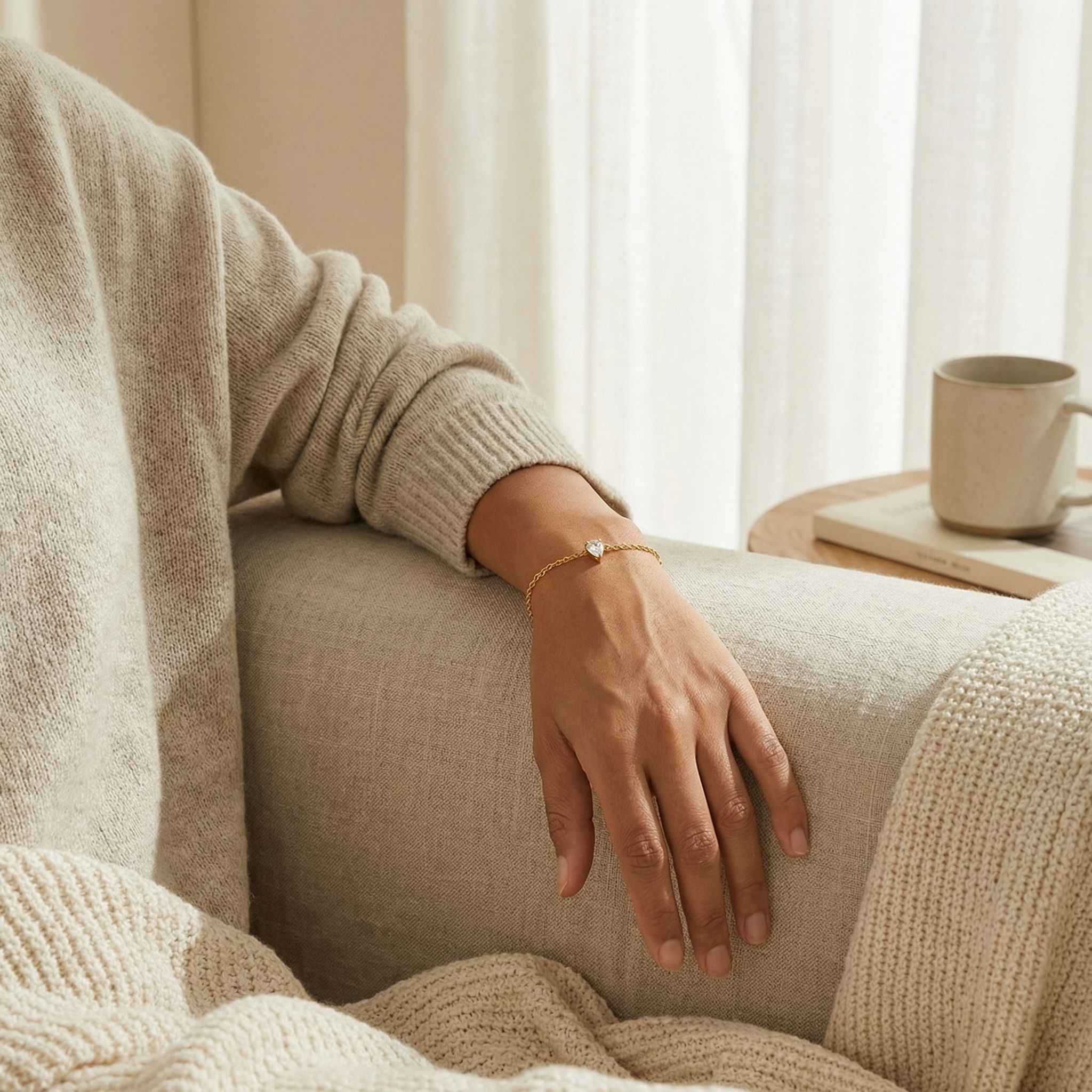 Person wearing a gold teardrop-shaped bracelet on a beige couch with a blurred background