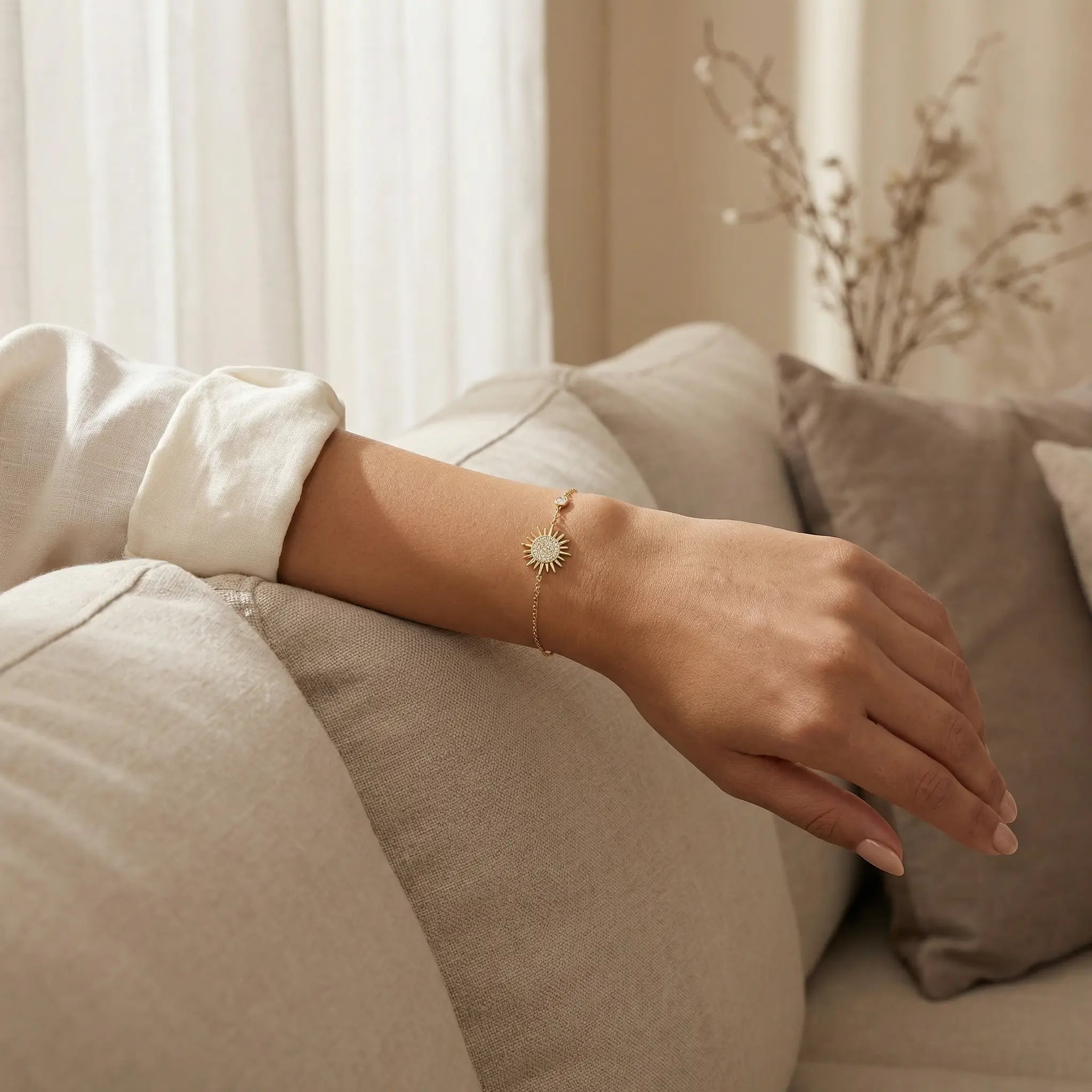 Hand wearing a delicate bracelet with sun-shaped pendant on a neutral background.