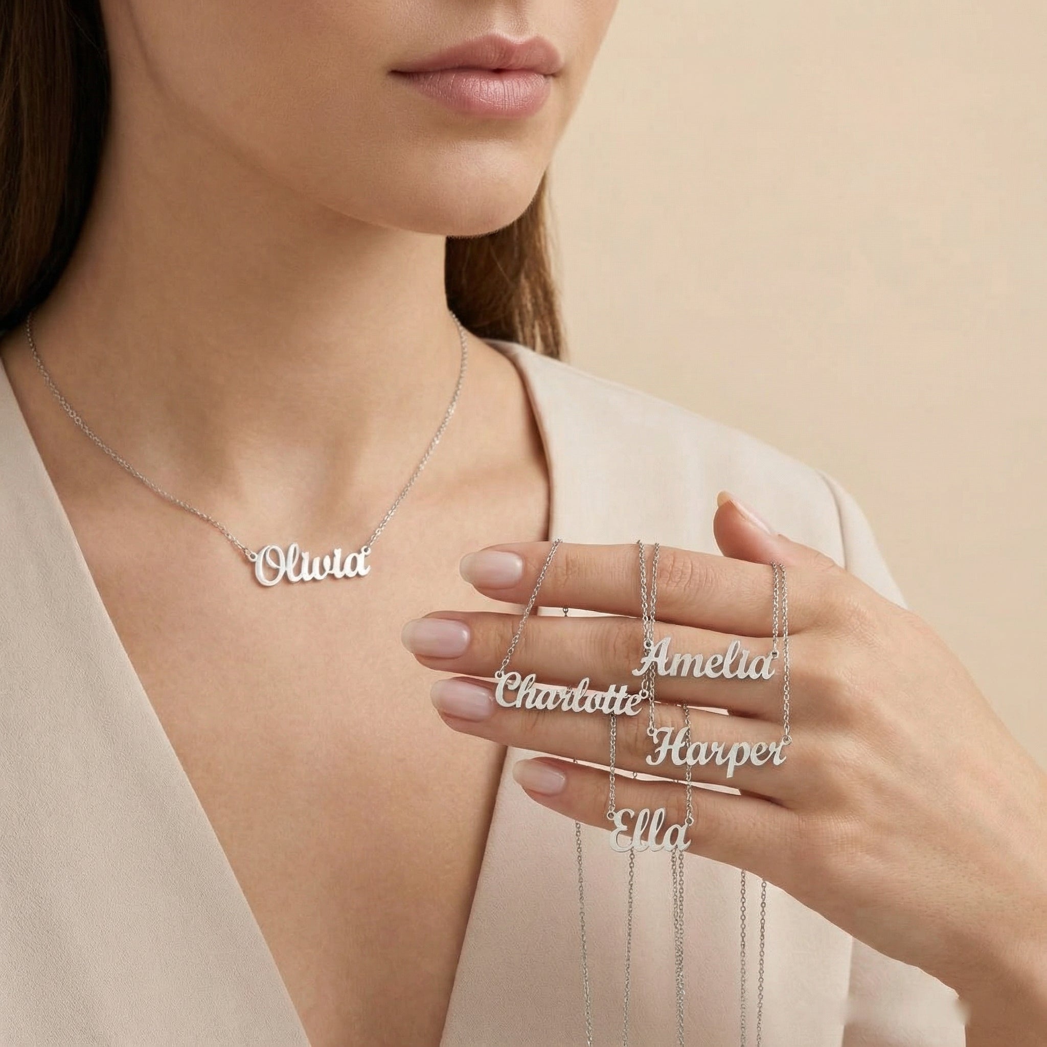 Person wearing a silver 'Olivia' necklace with other name pendants held in hand against a beige background