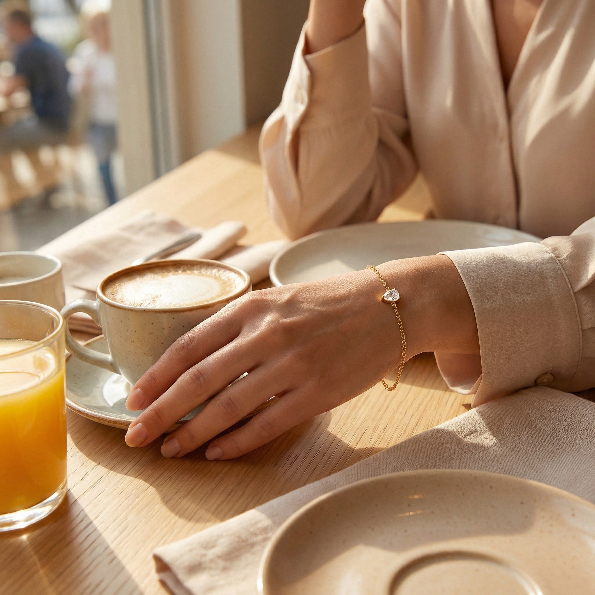 Person holding a cup of coffee at a table with a glass of orange juice and a teardrop-shaped bracelet