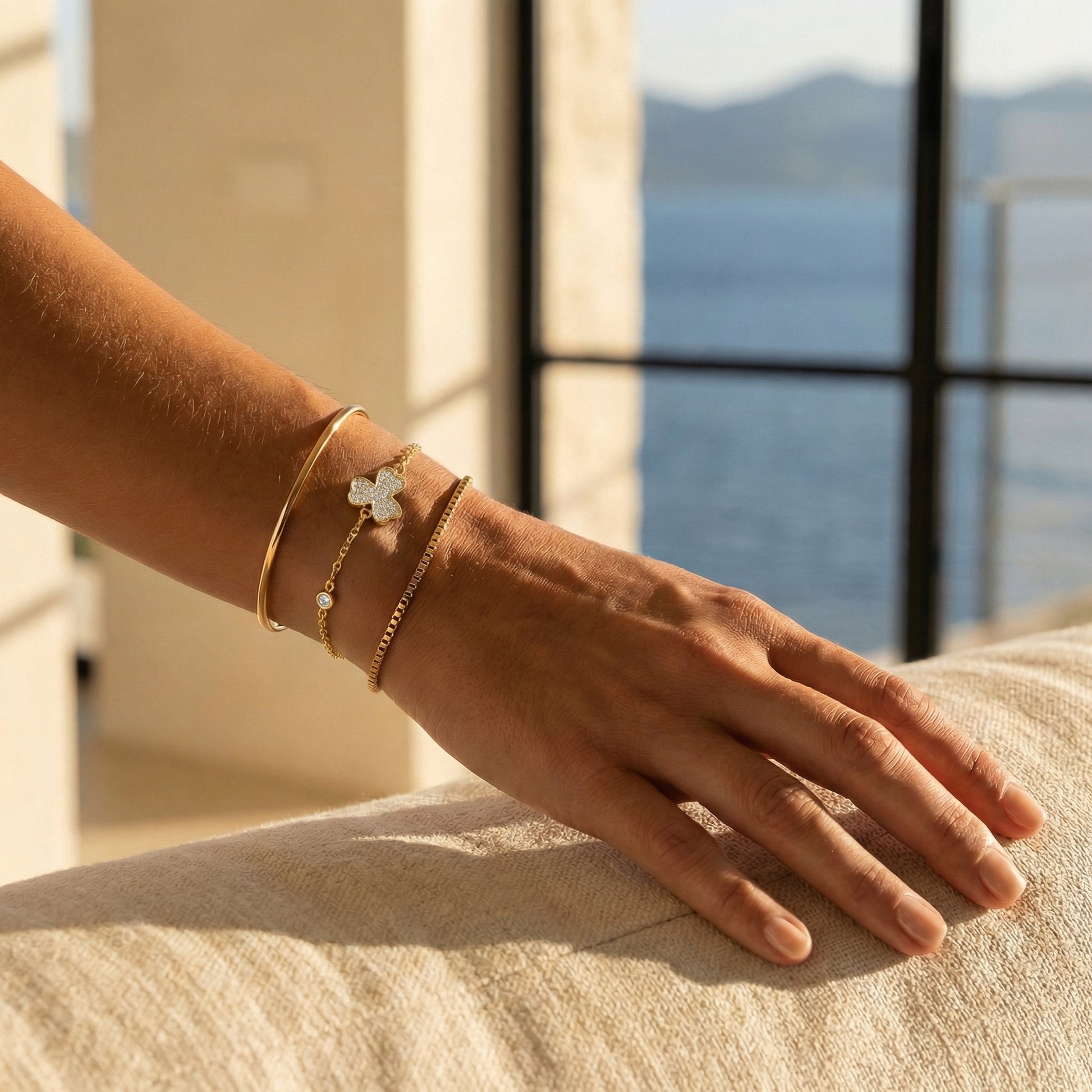 Hand wearing gold plated stacked bracelets with a scenic background