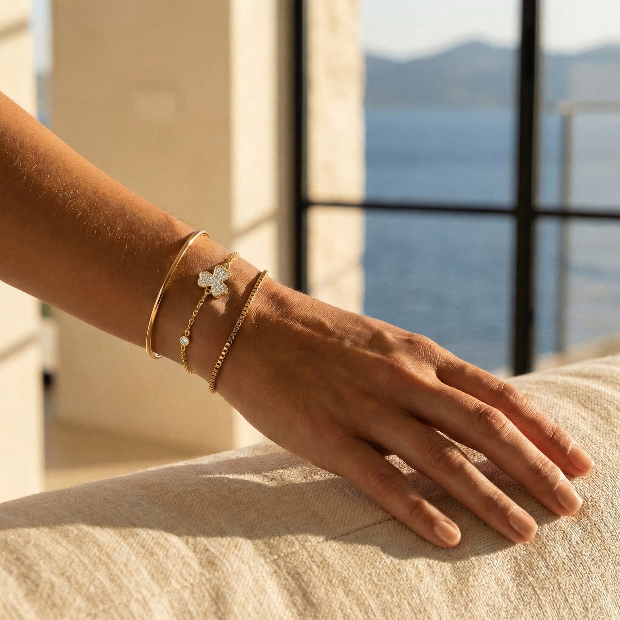 Hand wearing gold plated stacked bracelets with a scenic background