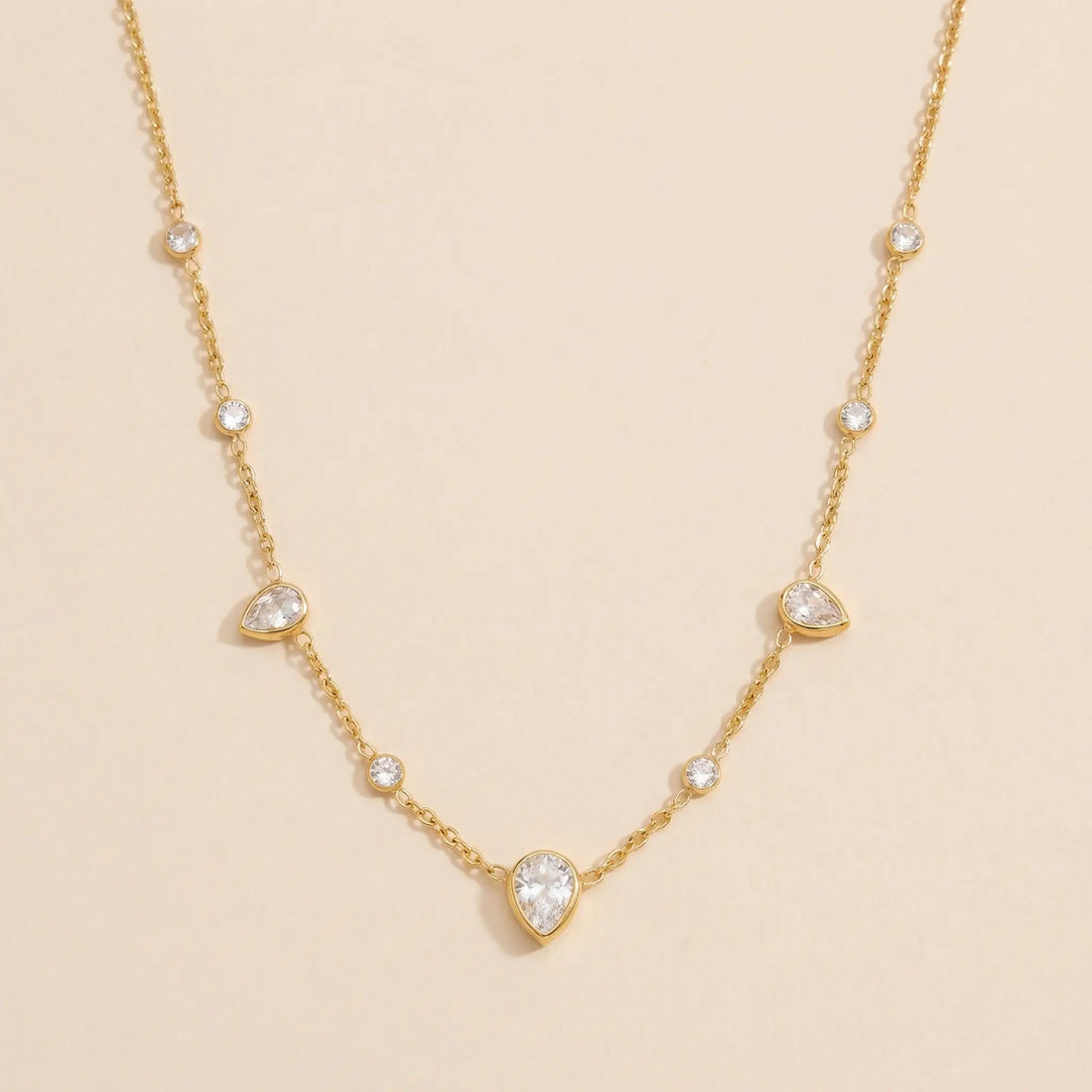 Gold necklace with teardrop-shaped gemstones on a beige background