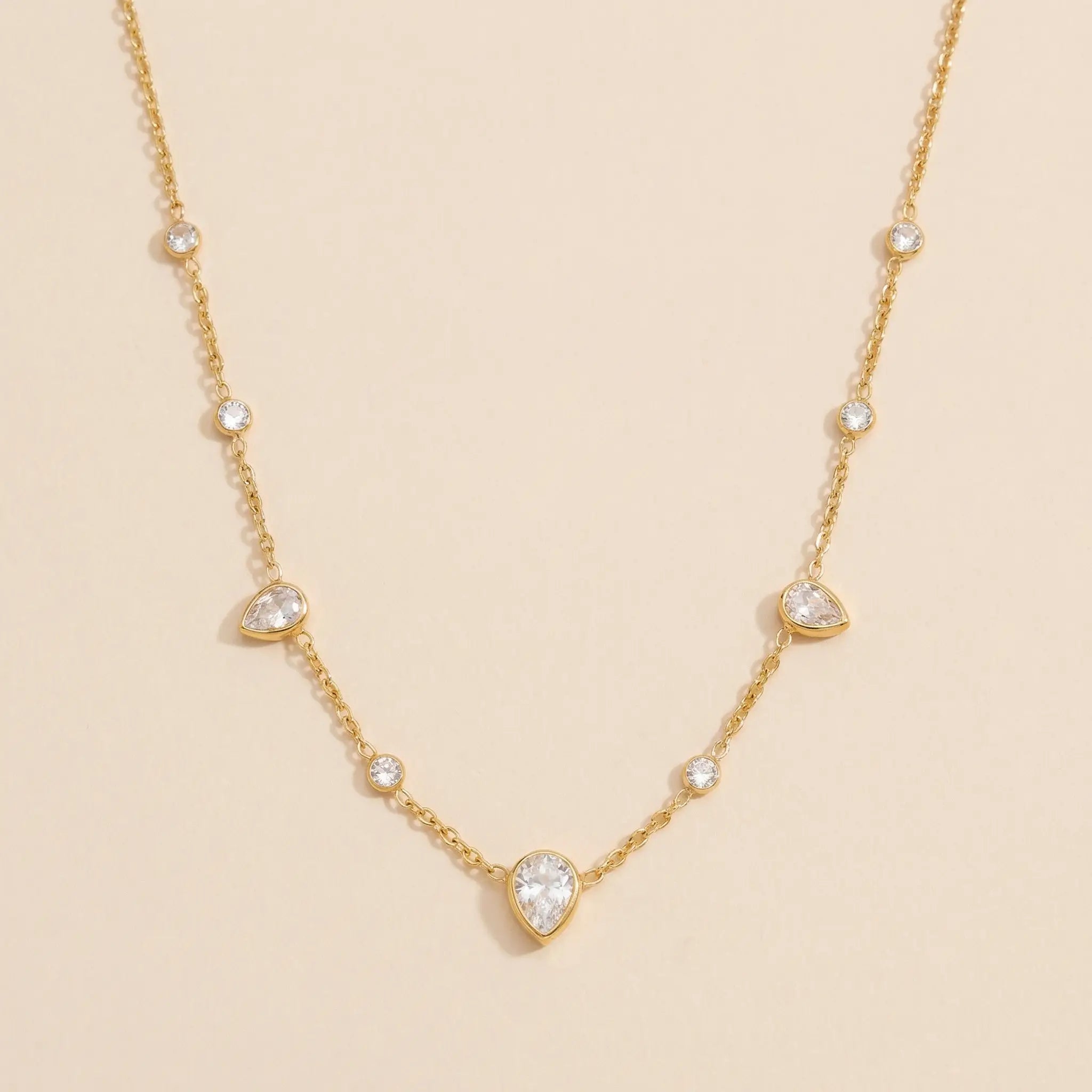 Gold necklace with teardrop-shaped gemstones on a beige background