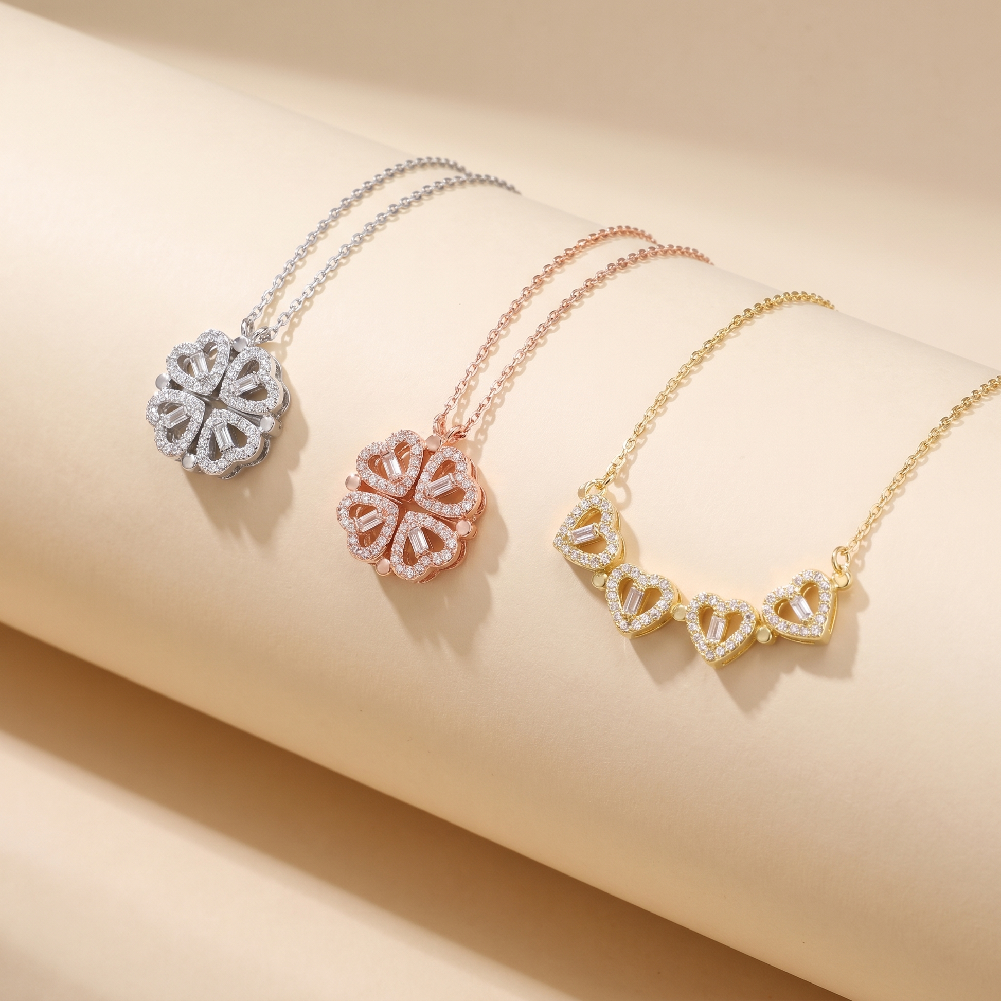 Lucky Heart necklace in gold, silver and rose gold finishes, flat lay on beige