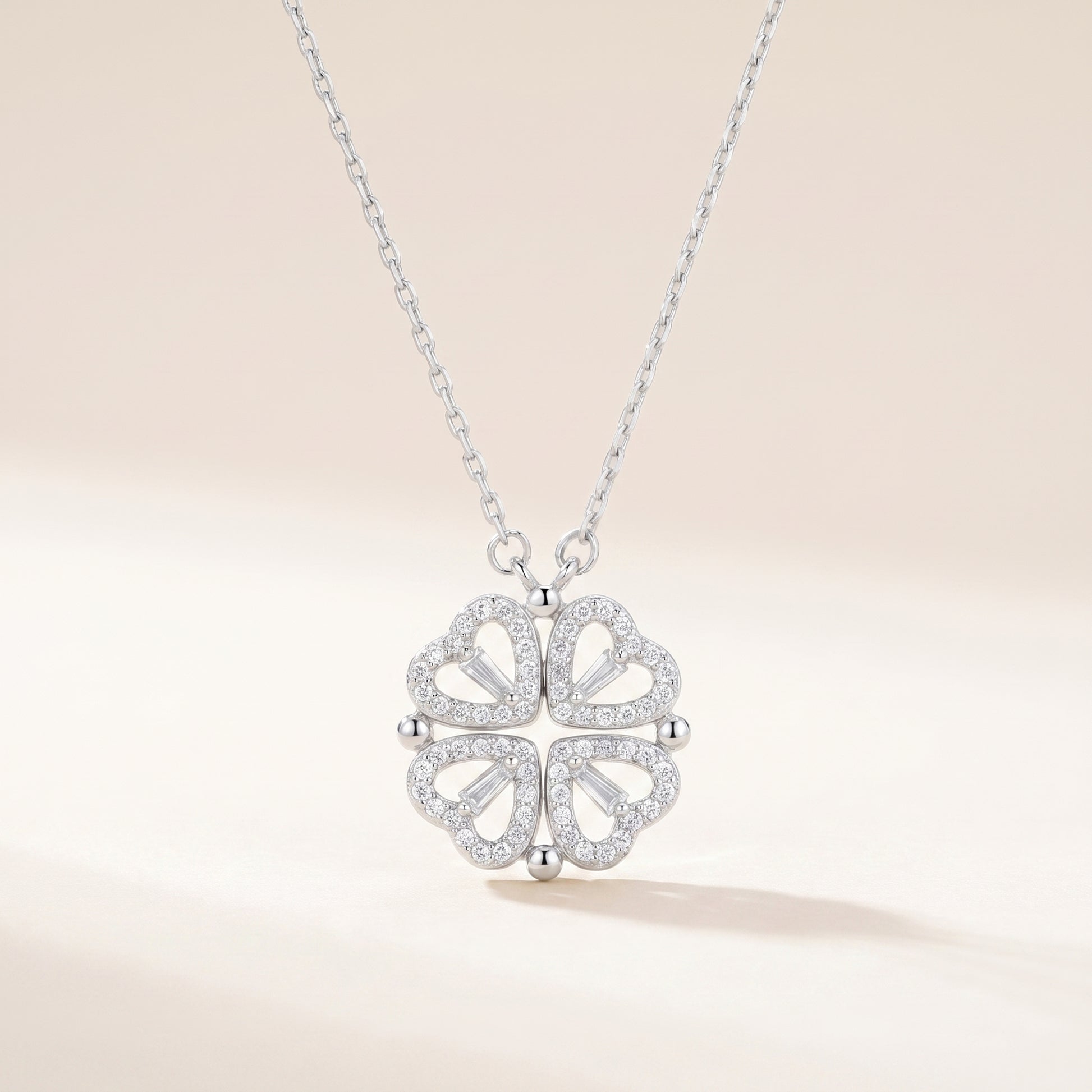 Silver four-leaf clover heart necklace with cubic zirconia on a soft beige background