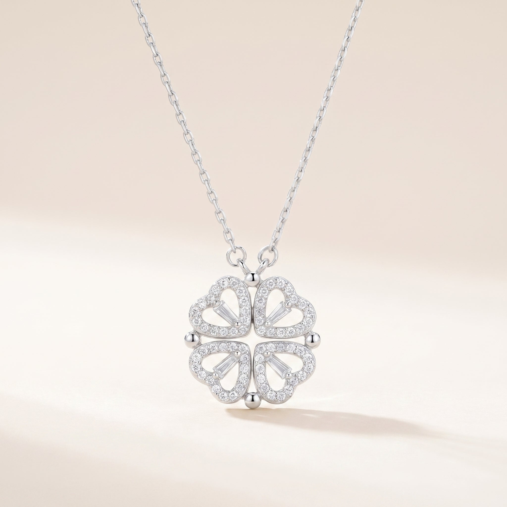 Silver four-leaf clover heart necklace with cubic zirconia on a soft beige background