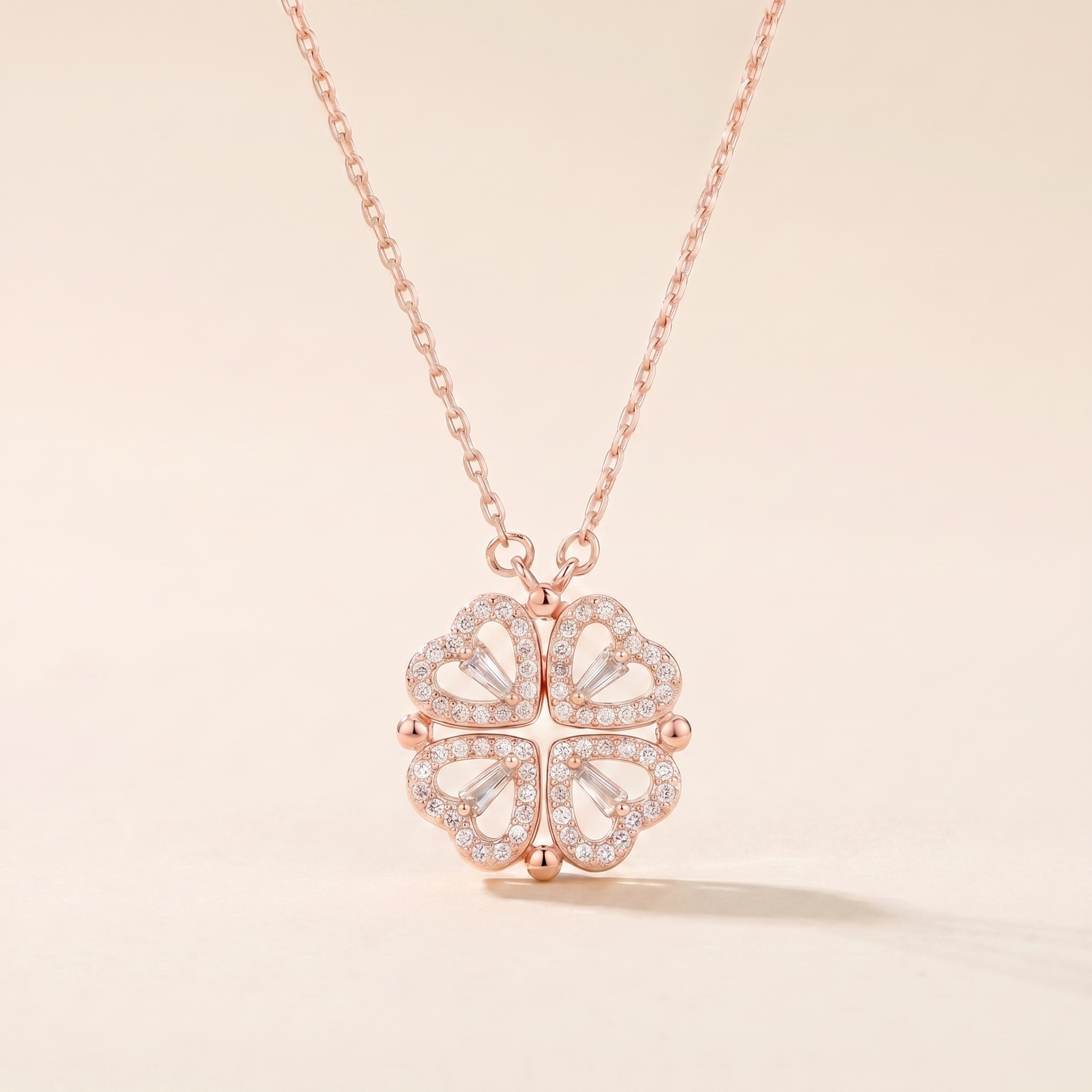Rose gold four-leaf clover heart necklace with cubic zirconia on a soft beige background