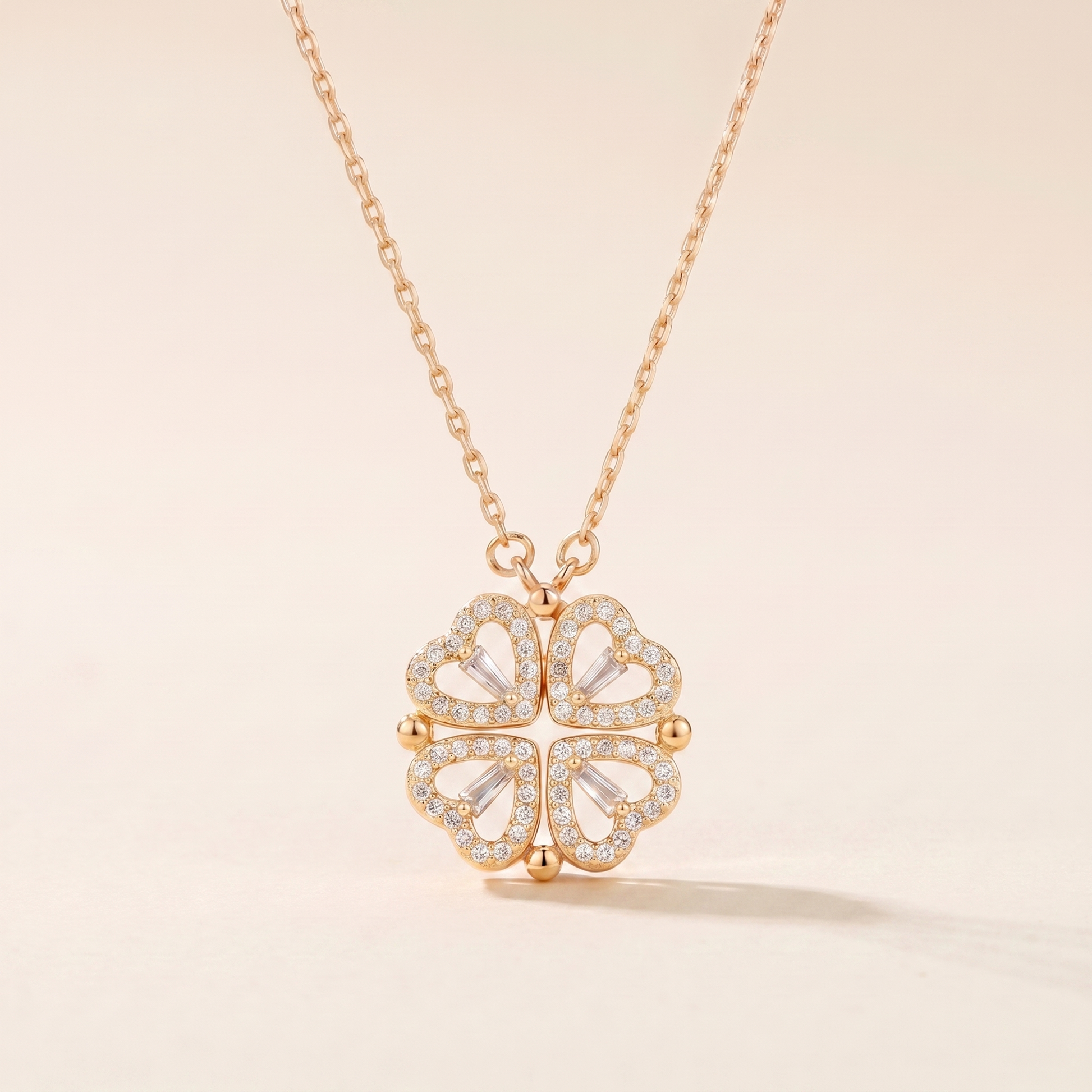 Gold four-leaf clover heart necklace with see-through cubic zirconia hearts on a soft beige background