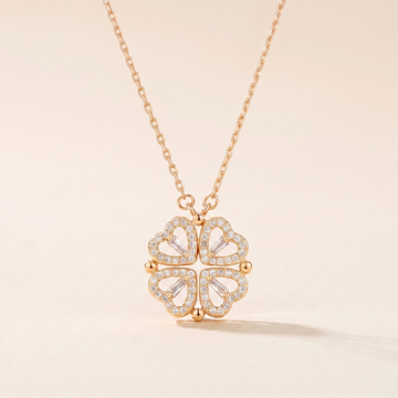 Gold four-leaf clover heart necklace with see-through cubic zirconia hearts on a soft beige background