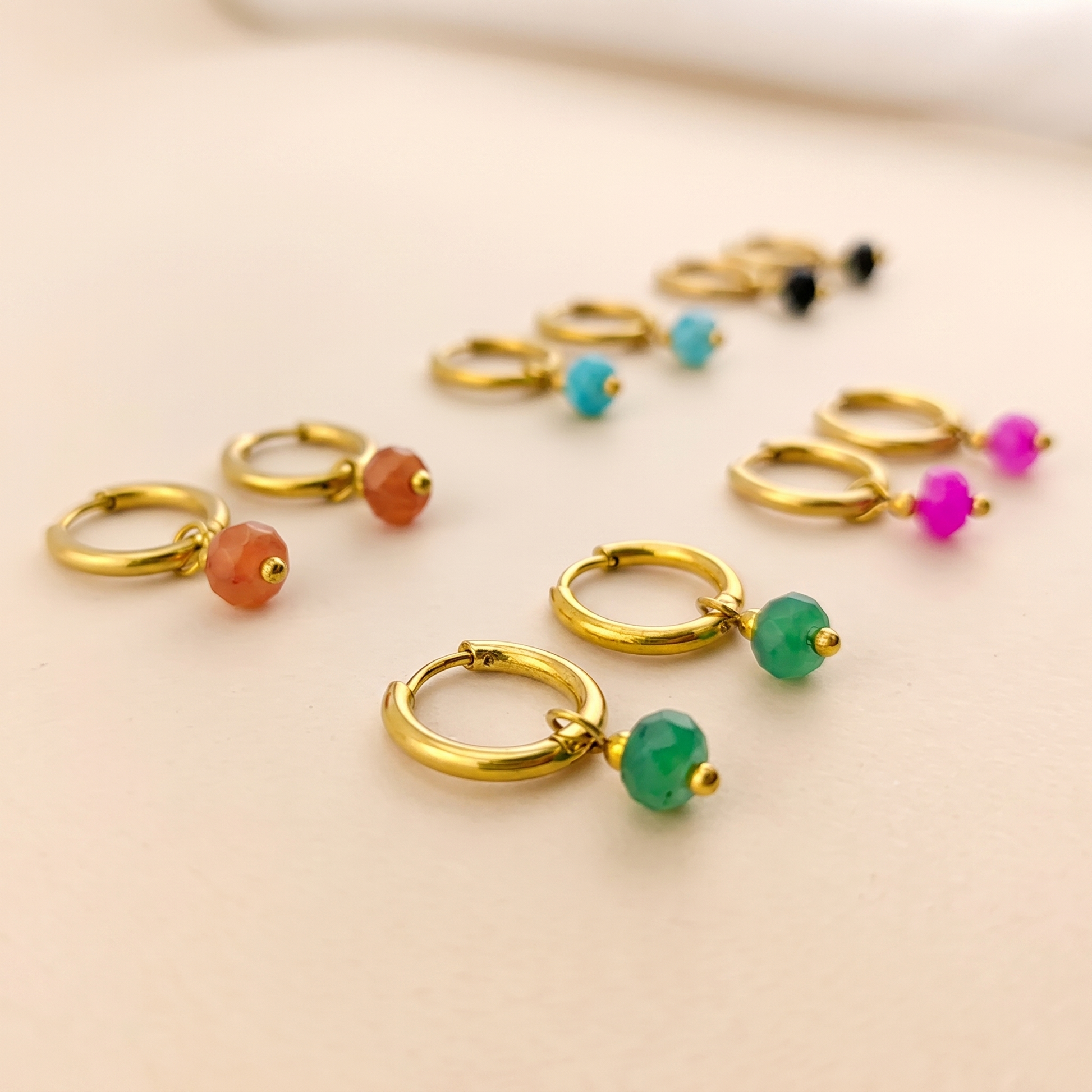 Gold-tone natural stone huggie hoop earrings on a soft beige background