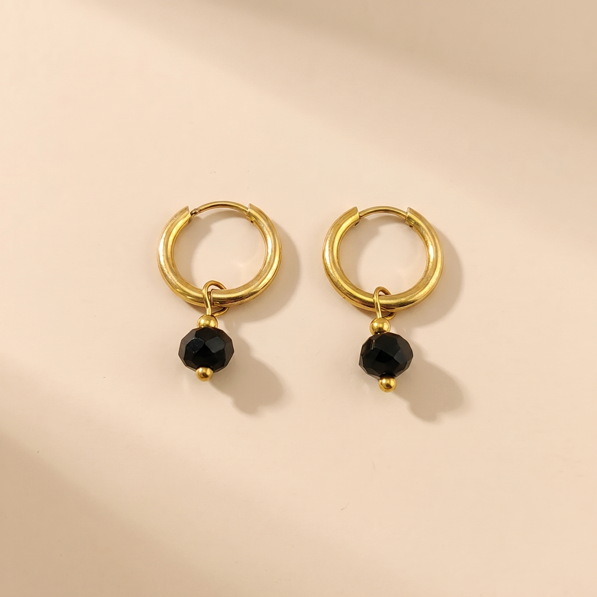 Gold-tone huggie hoop earrings with black natural stone on a beige background