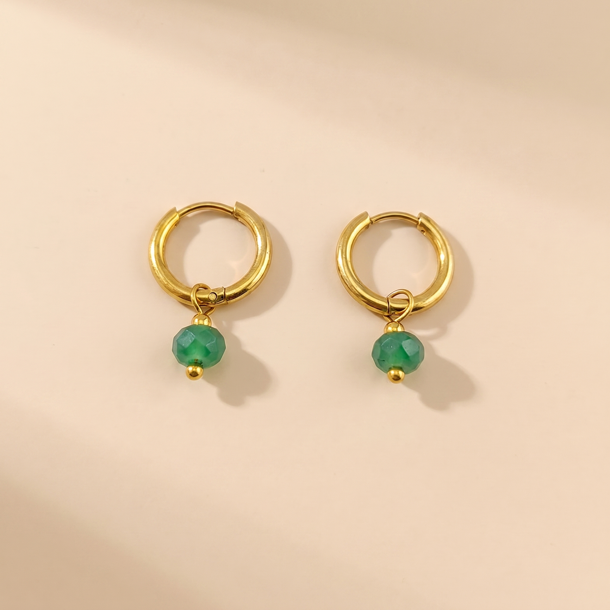 Gold-tone huggie hoop earrings with green natural stone on a beige background