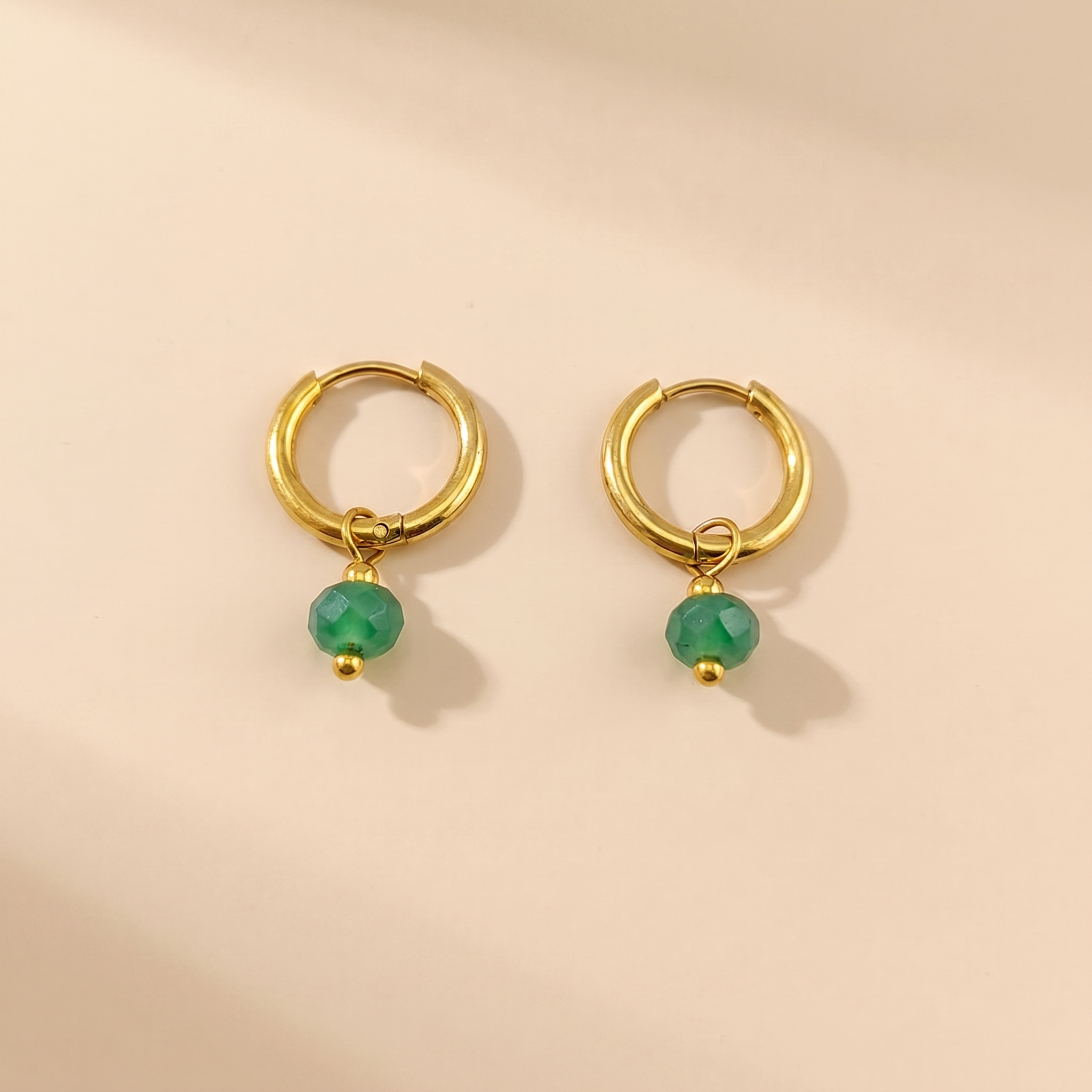Gold-tone huggie hoop earrings with green natural stone on a beige background