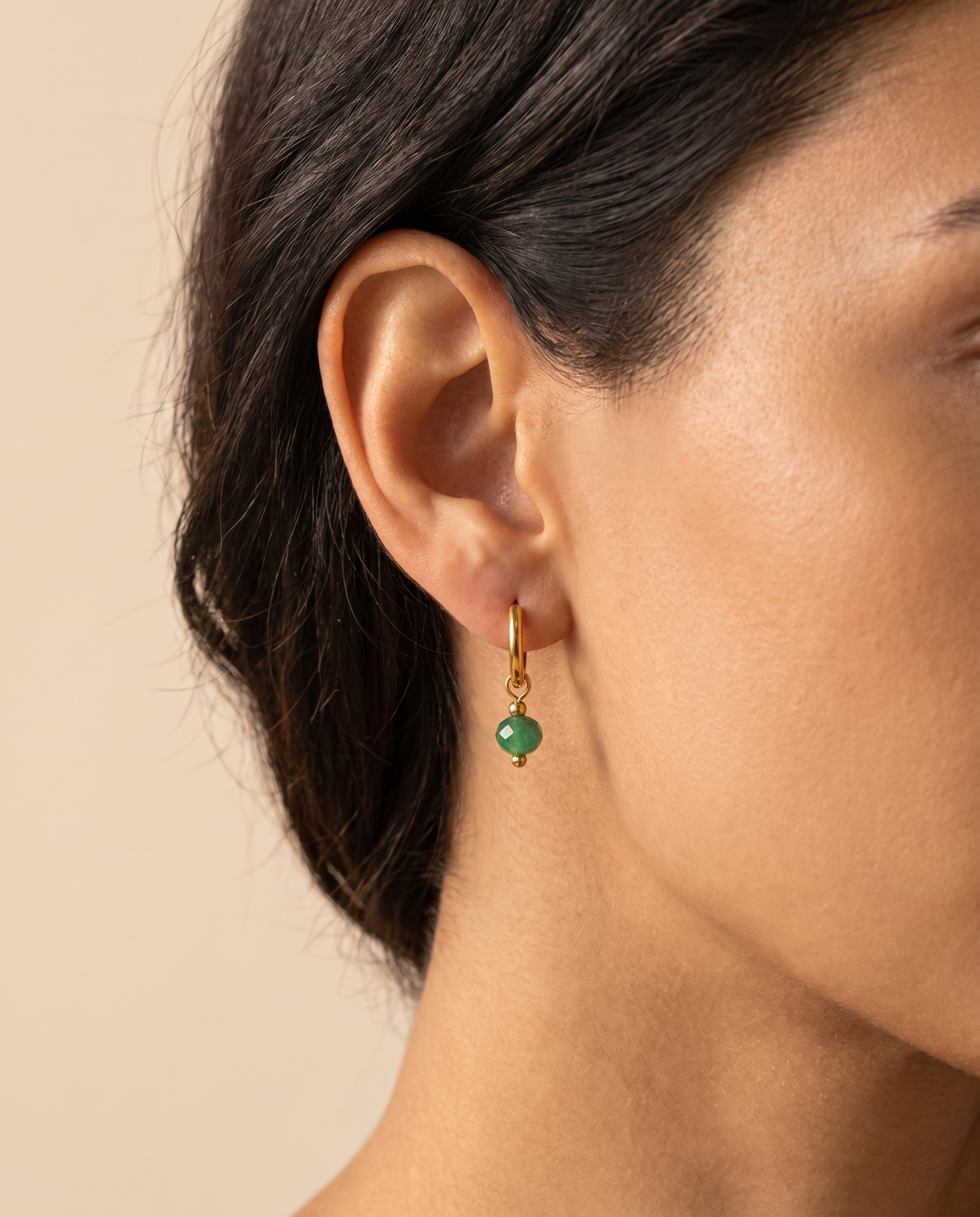 Woman wearing a gold-tone huggie hoop earring with a natural green stone